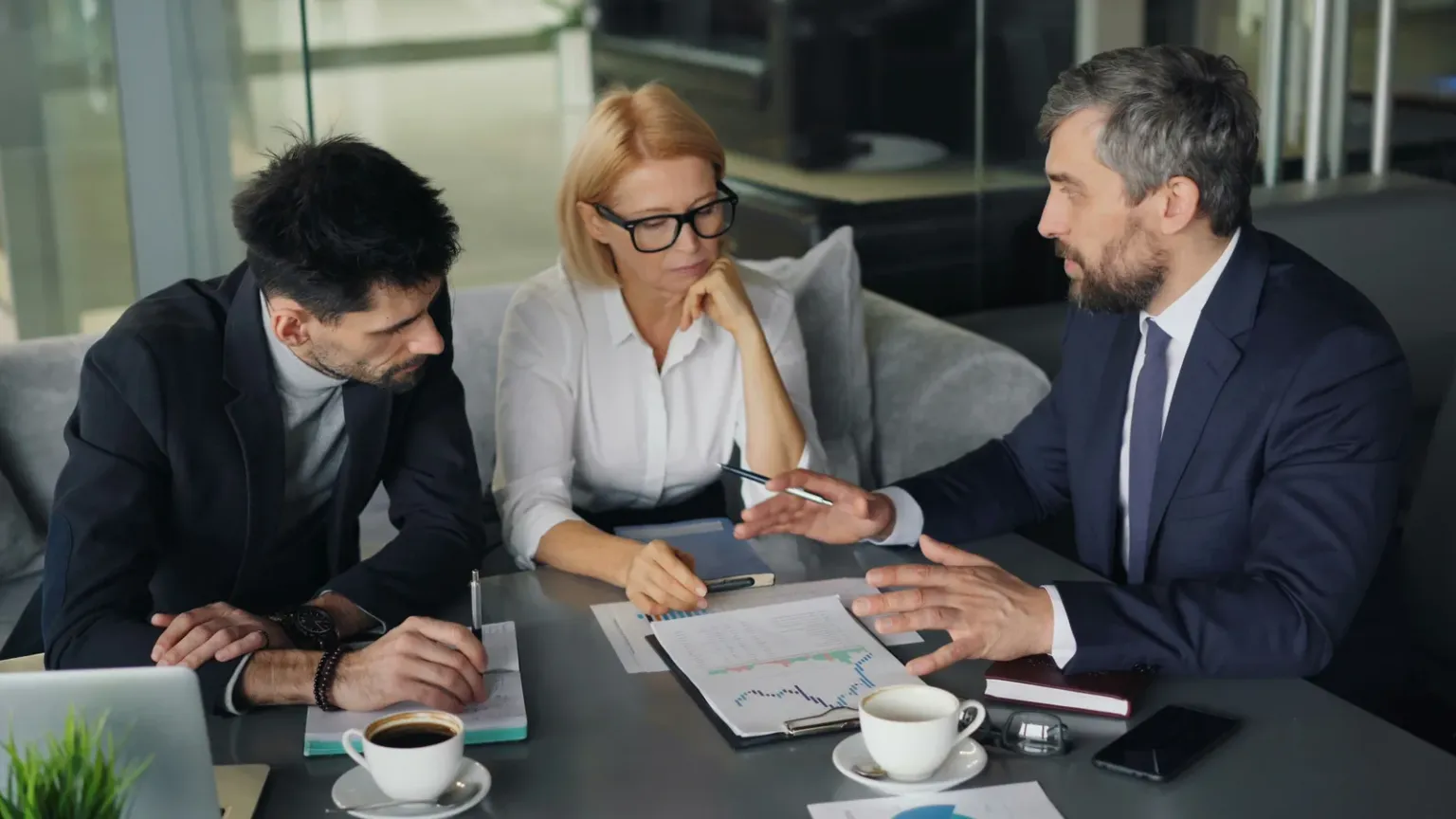 Three people seated around a table discussing printed documents and charts.