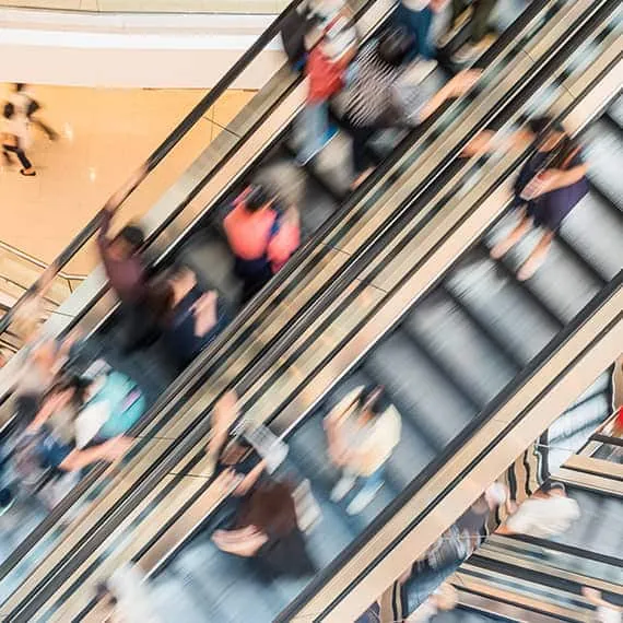 Shoppers riding escalators in a busy mall