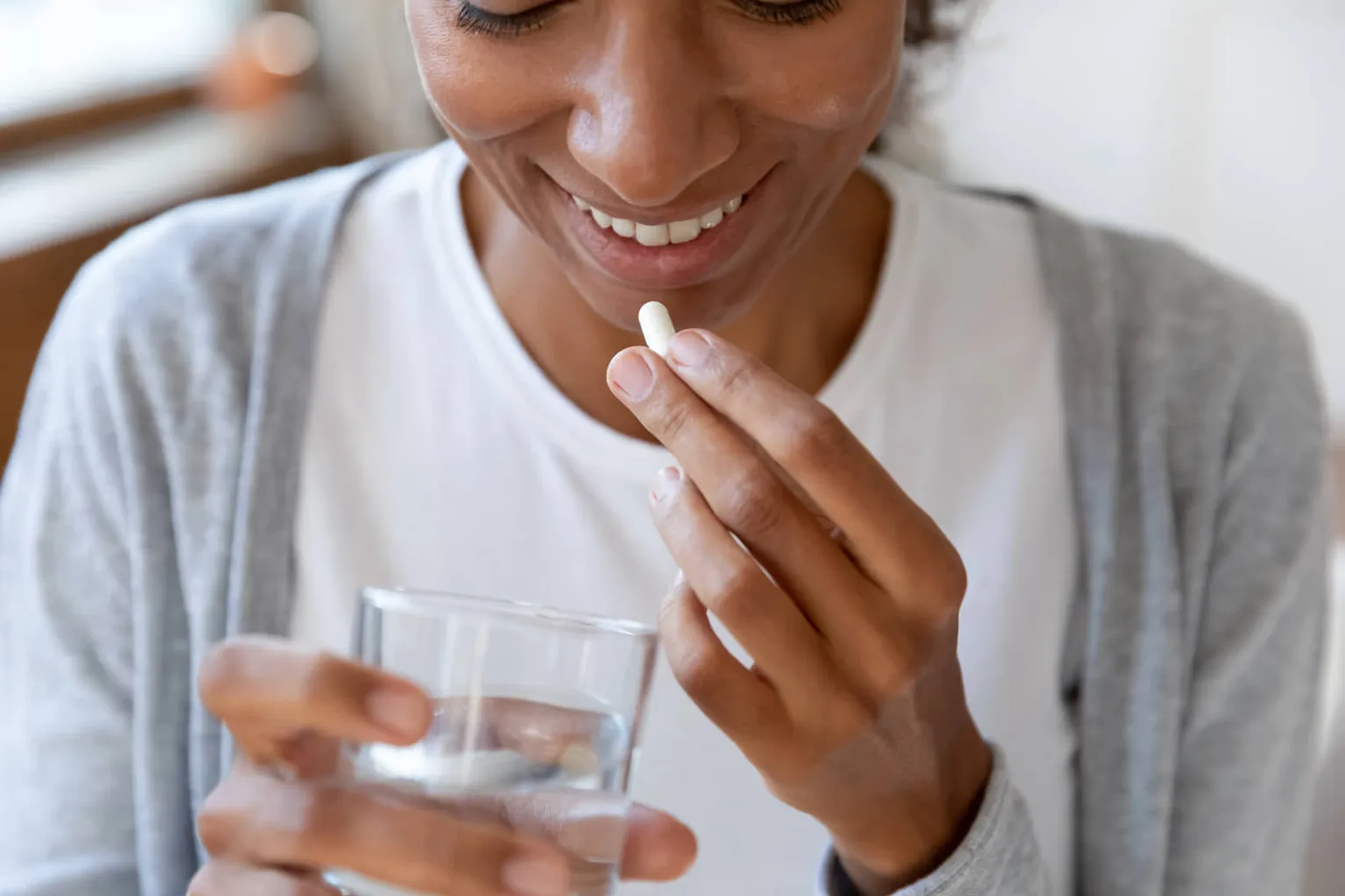 Woman holding a pill and a glass of water