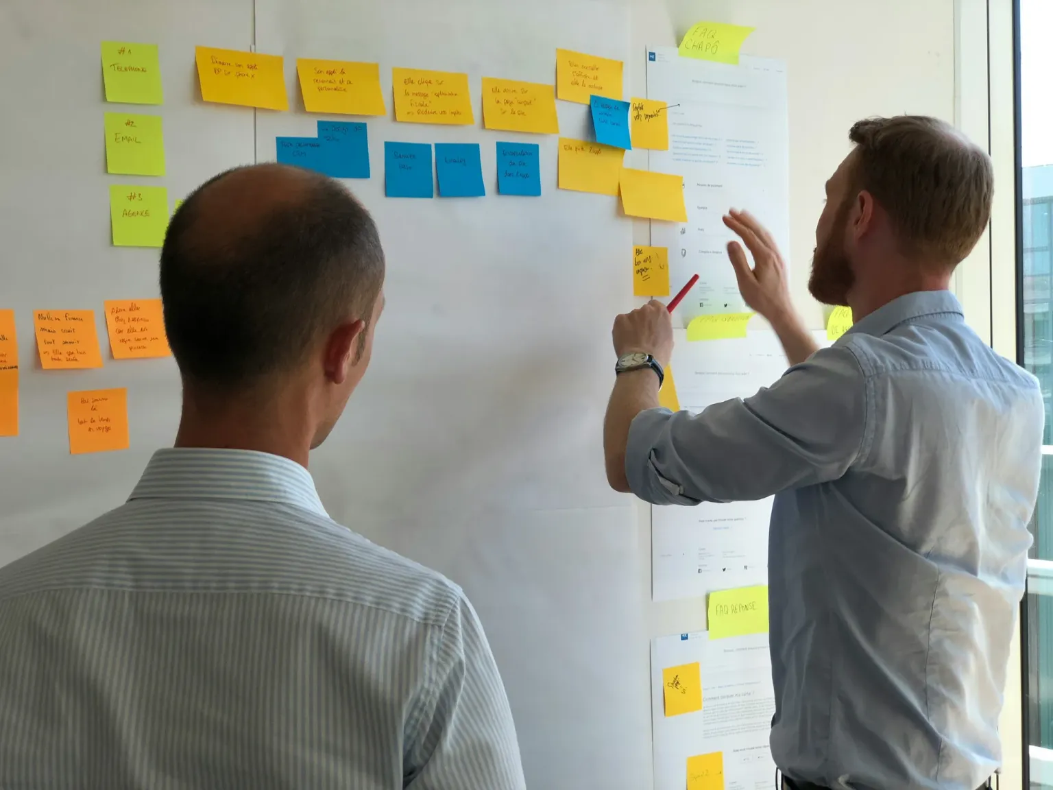 Two people reviewing sticky notes and research materials on a wall