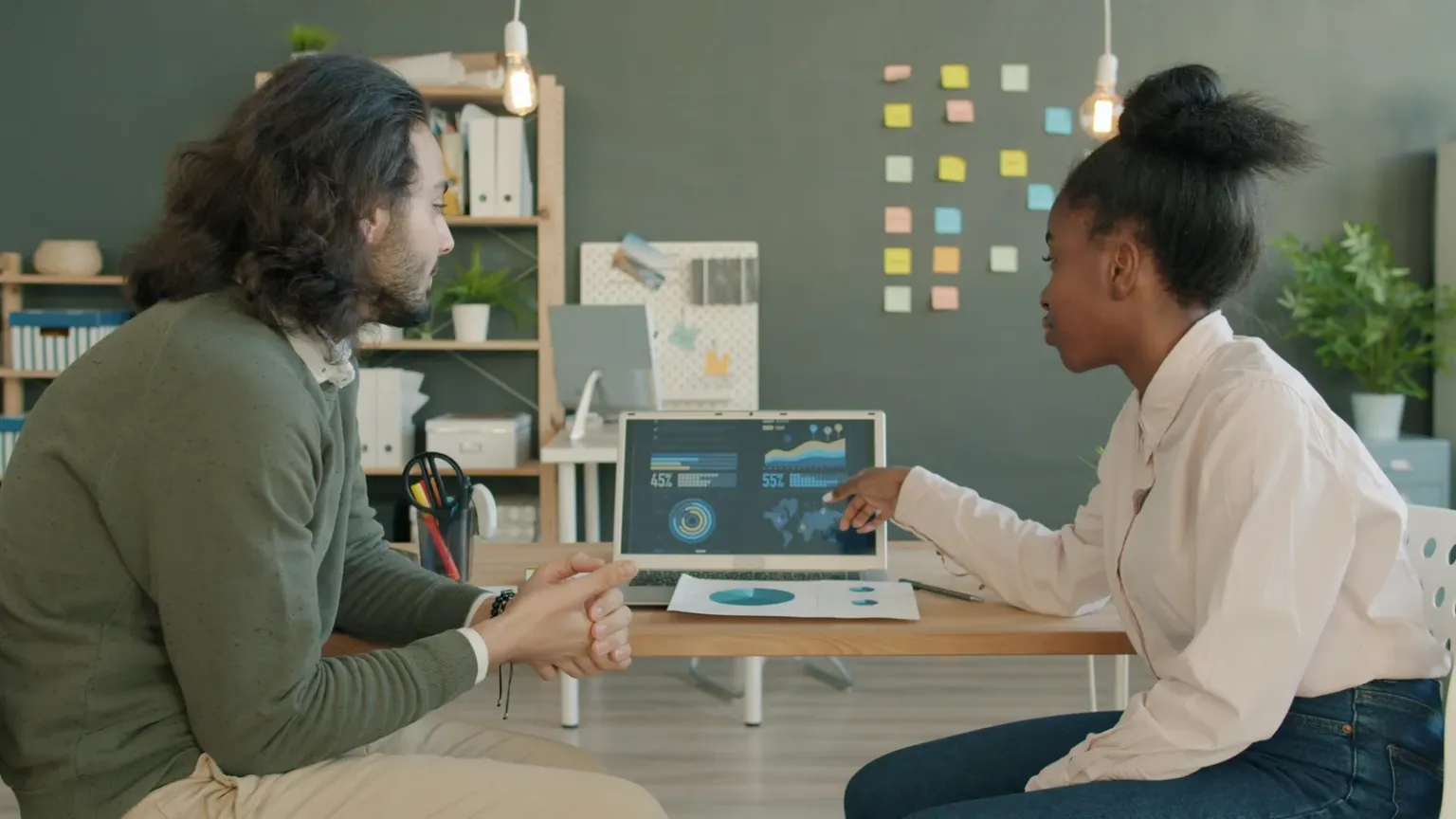 Two people seated at a desk discussing charts on a laptop screen.