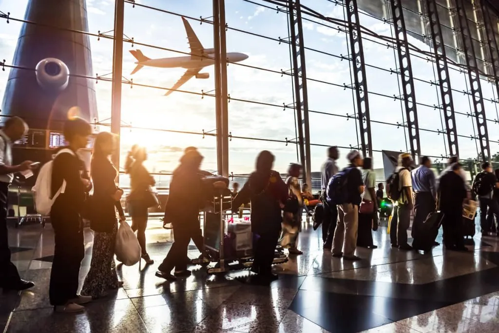 Travelers in an airport terminal as a plane takes off outside