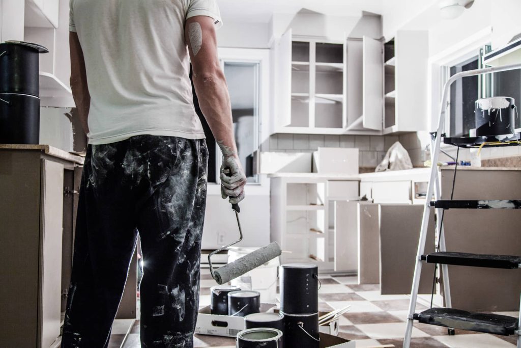 Person holding a paint roller beside kitchen cabinets